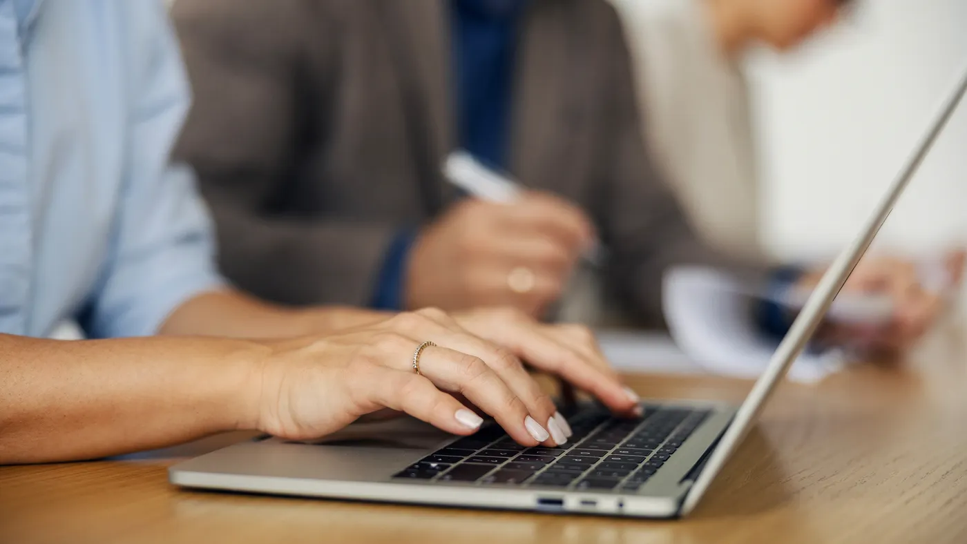 Woman's hands typing on a laptop during a corporate meeting, collaborating with colleagues and doing office work