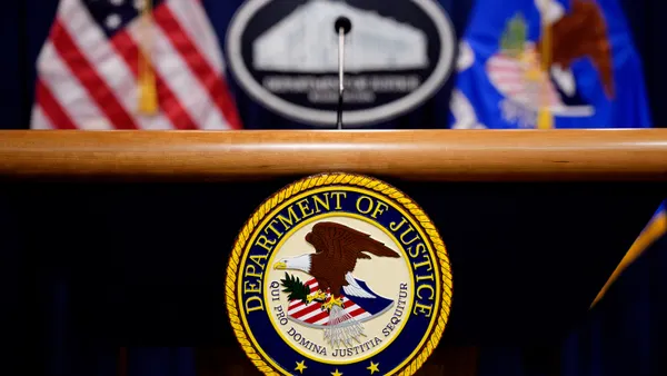 The seal of the U.S. Department of Justice hangs from the front of a lectern.