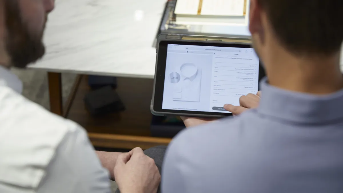 Two people sit with an iPad looking at a dress shirt.