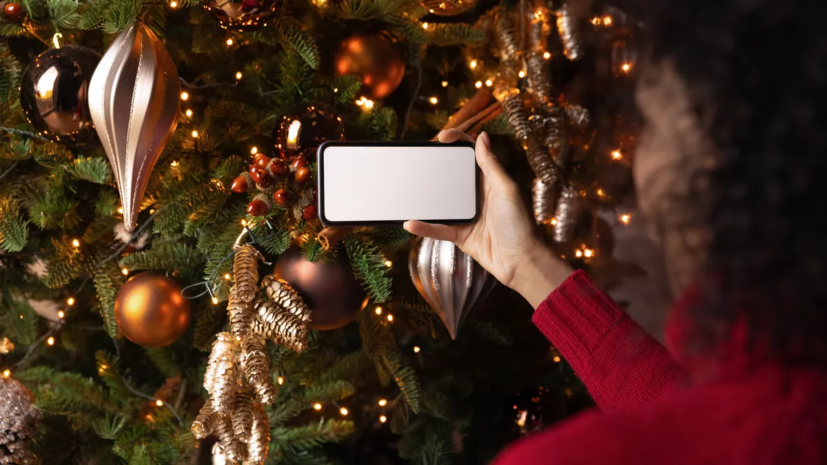 Person holding a mobile phone in front of a Christmas tree.