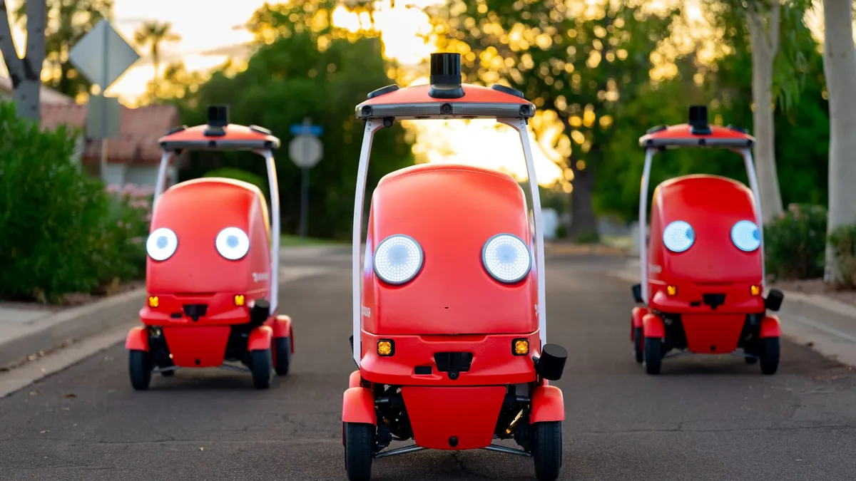 An image of three red robots with two eyes on a street.