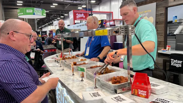 A worker offers a sample of Tater Kegs potato snacks to a show attendee