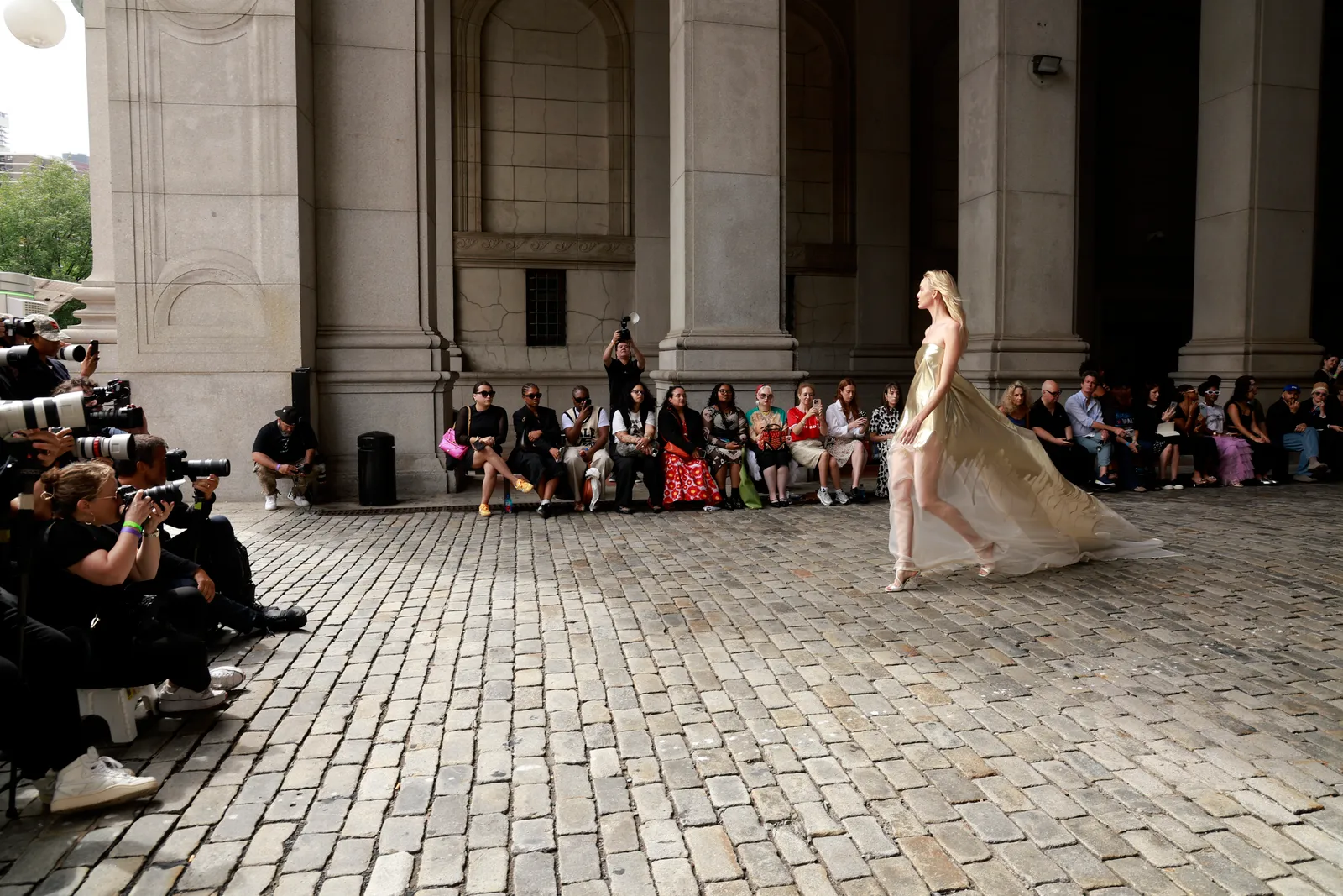 A model in a sheer cream dress walks down a runway.