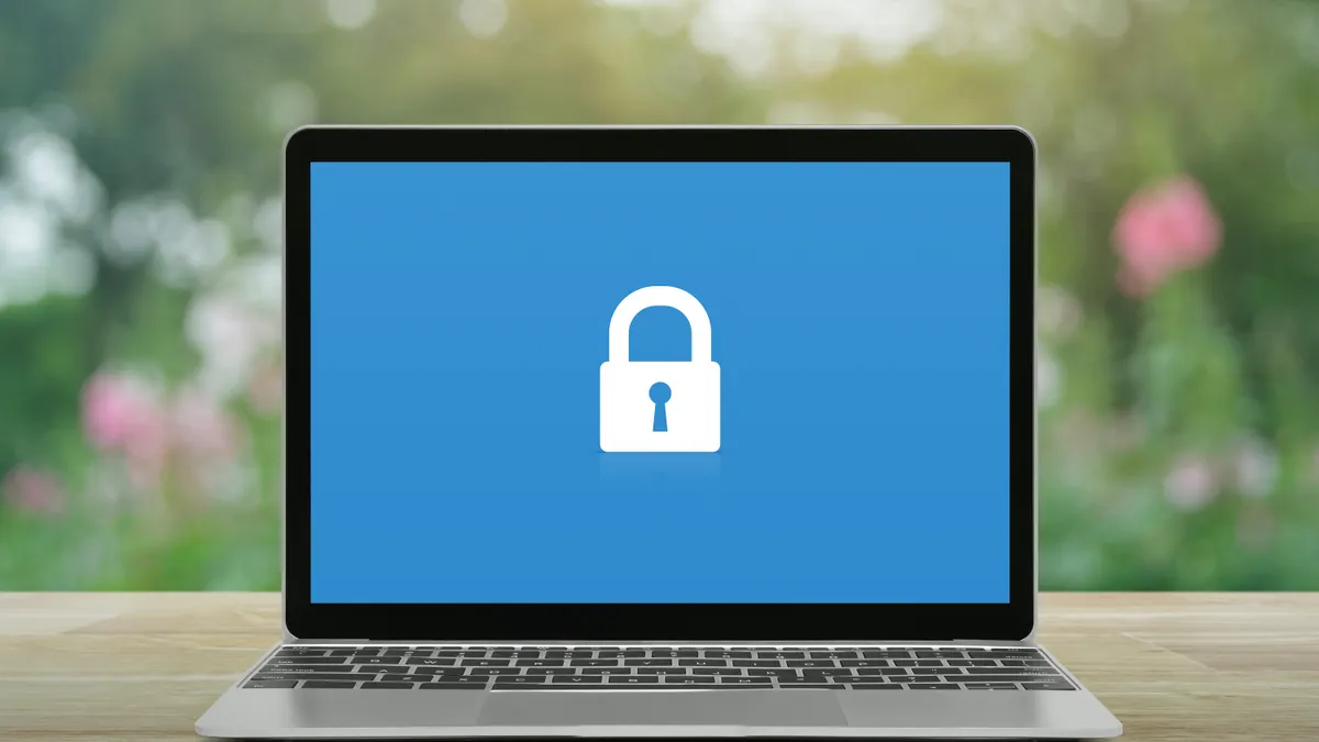 A padlock icon on modern laptop computer monitor screen sits on wooden table.