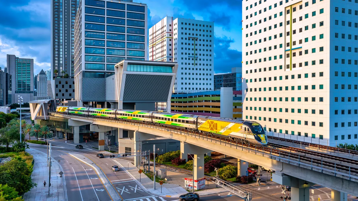 A view of the Miami skyline with tall buildings and a modern passenger train emerging from an elevated station.