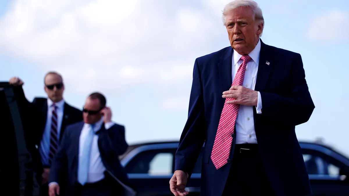 President Donald Trump walks while adjusting his tie.