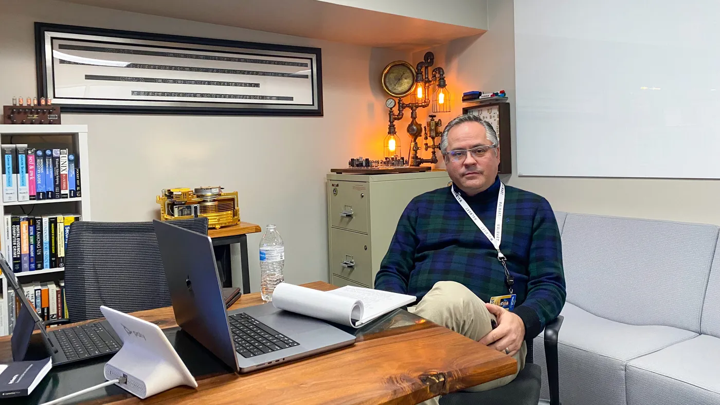 Man sits in an office with technical instruments in the background.