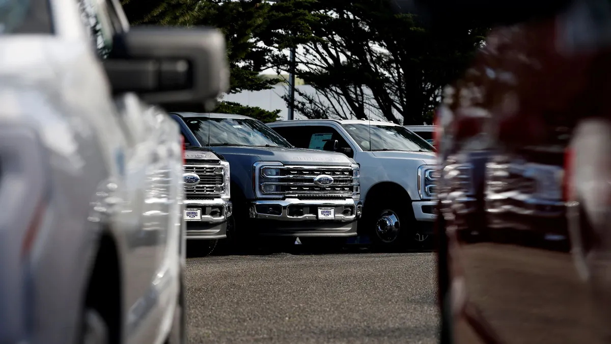 Two vehicles are parked side by side while a lineup of Ford trucks is parked in the background.