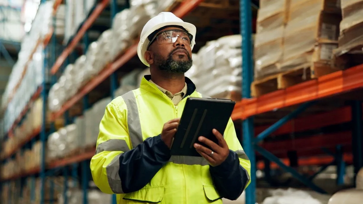 Black man with helmet and tablet at warehouse for distribution industry.