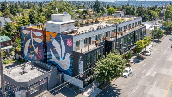 A long apartment building with two murals depicting a bird and a flower.