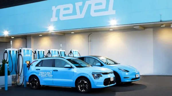 Two blue Revel EVs next to charging stations.