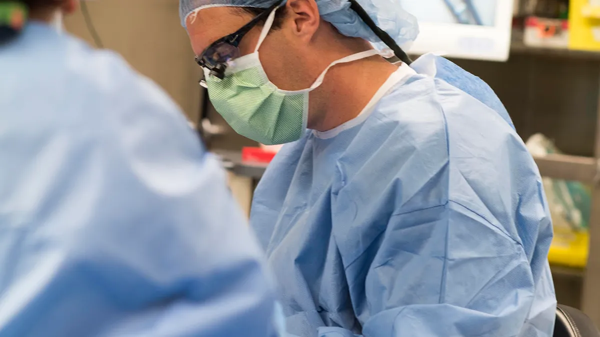 George Magrath wears blue scrubs and sits over a patient.