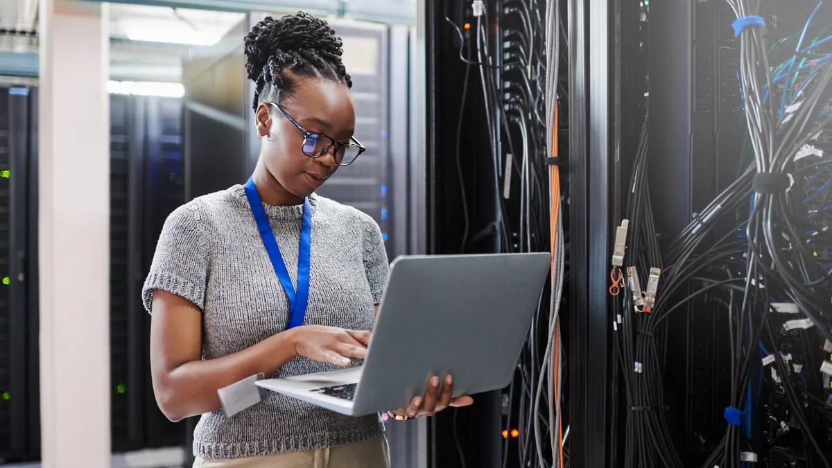 Shot of a young woman using a laptop in a server room.