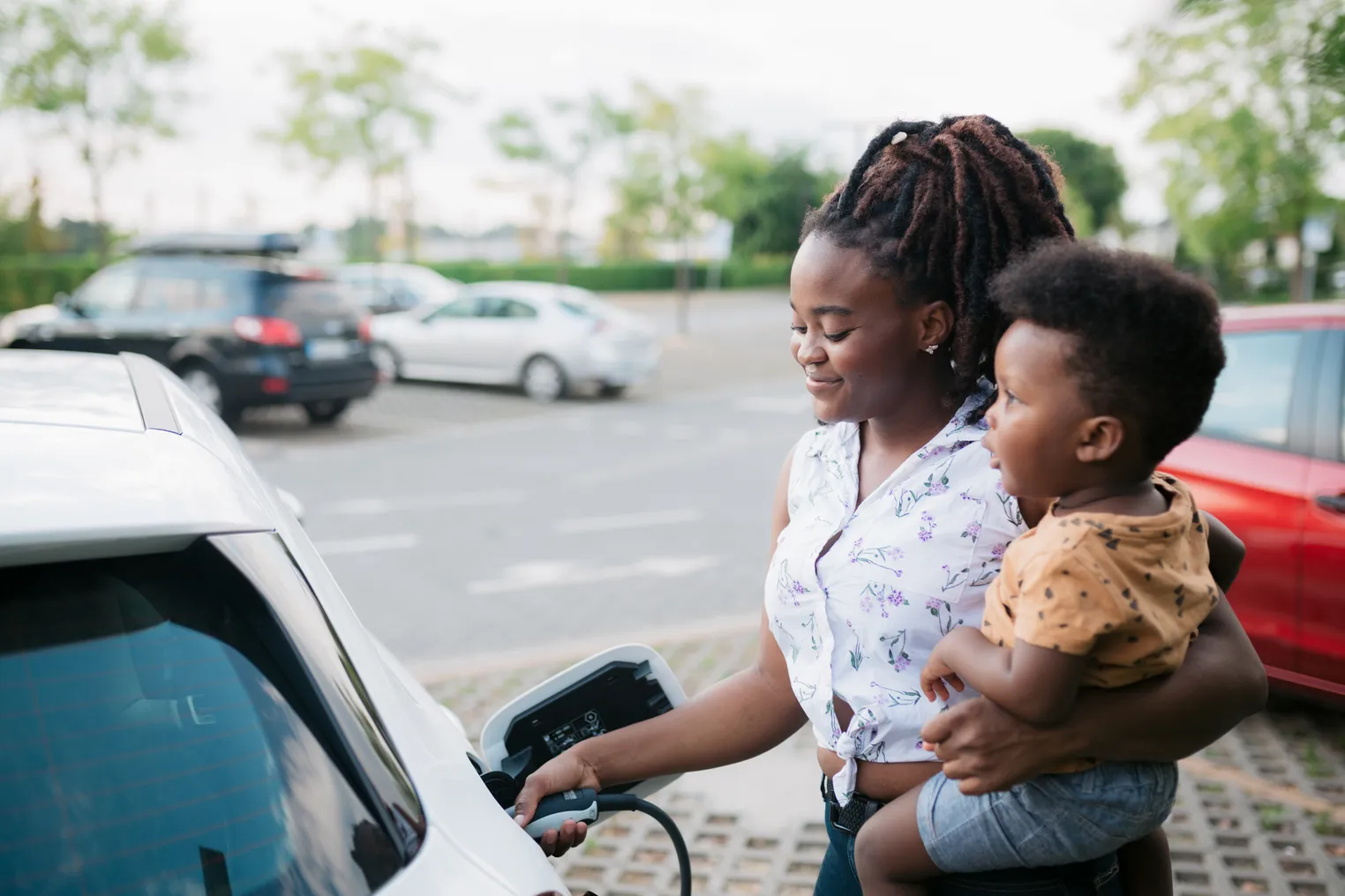 A woman charging her electric car and holding her baby.