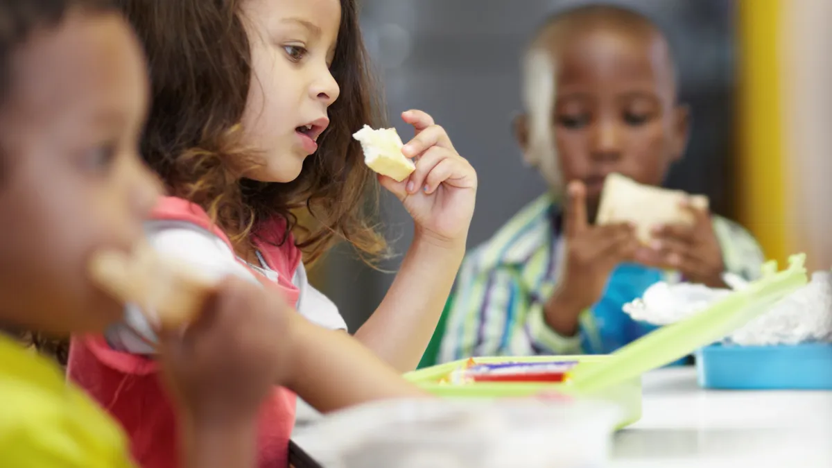 Three young students eat lunch together at school.