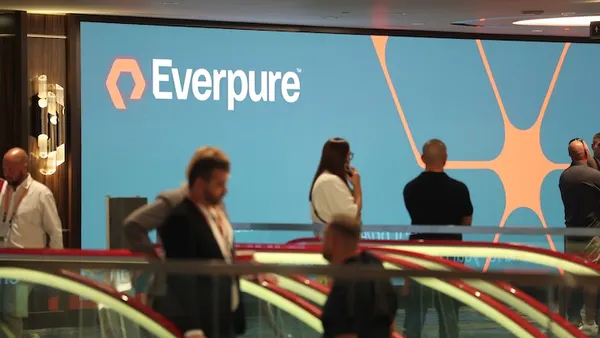 Attendees at a conference hosted by Everpure ride an escalator near a sign bearing the technology company's logo.