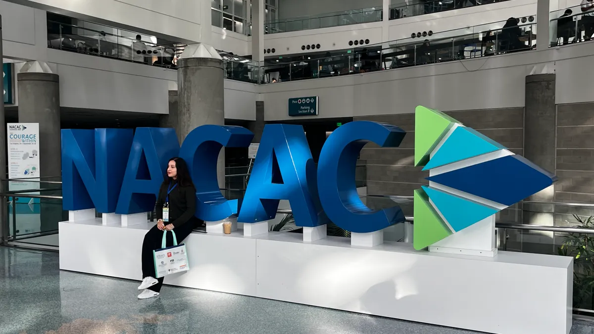 A person posed in front of a large display structure reading "NACAC."