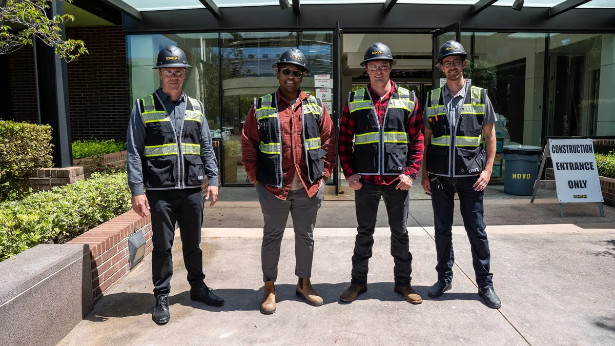 Four construction workers stand in front of a building entrance.