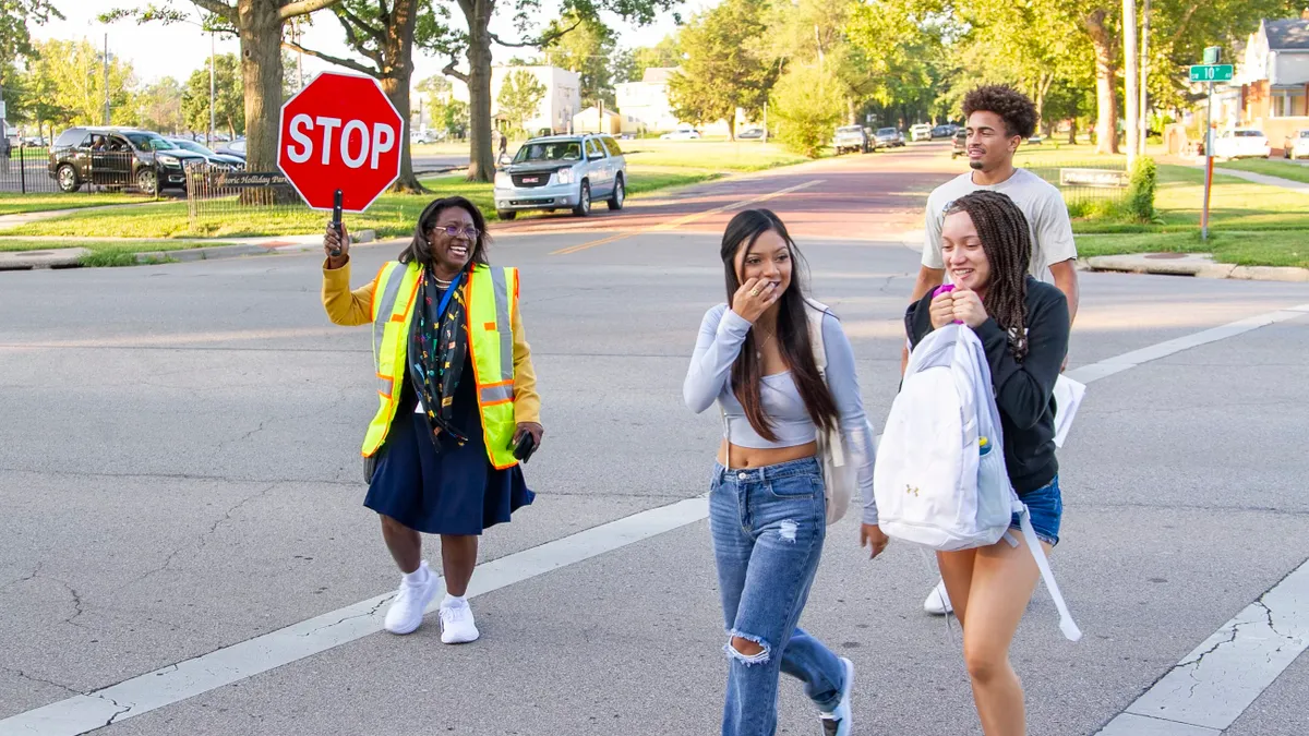 Topeka Superintendent Tiffany Anderson holds up a stop sign while serving as a crossing guard on a school day. Three students are shown crossing the street.