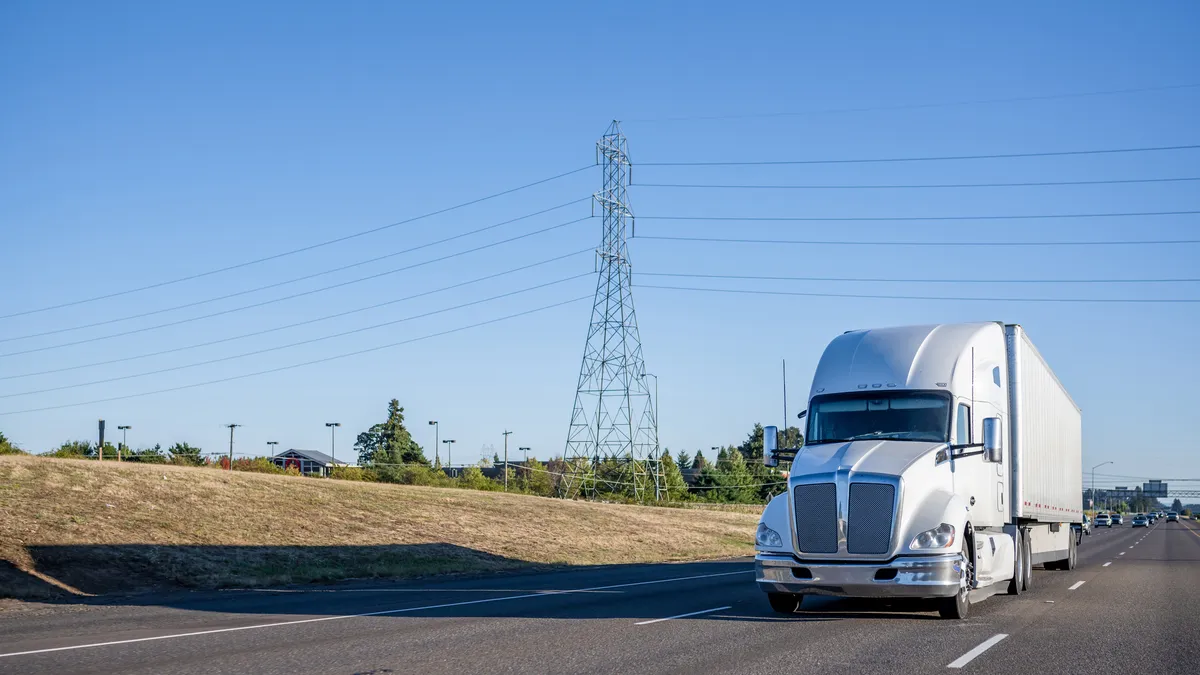 A tractor-trailer travels on a multi-lane highway with passenger vehicles in the background.