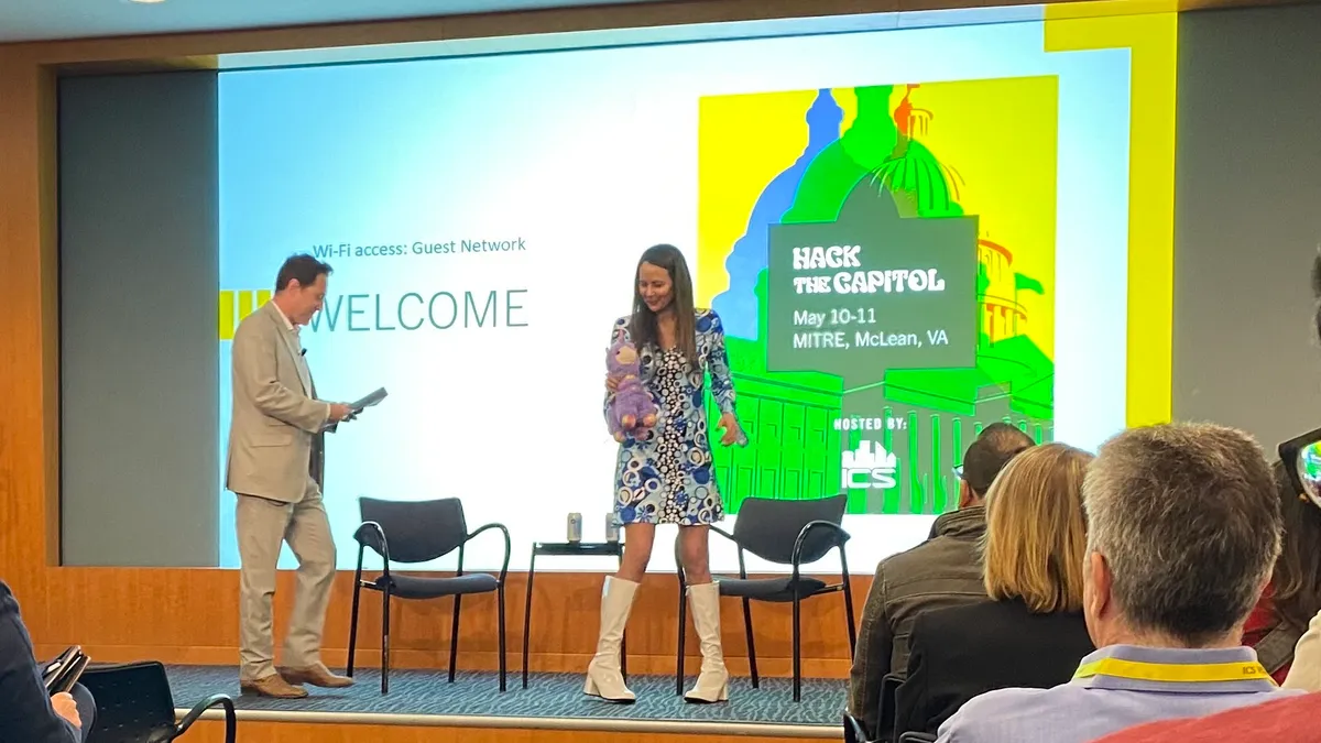 Woman and a man standing on stage in front of a screen that says Hack the Capitol