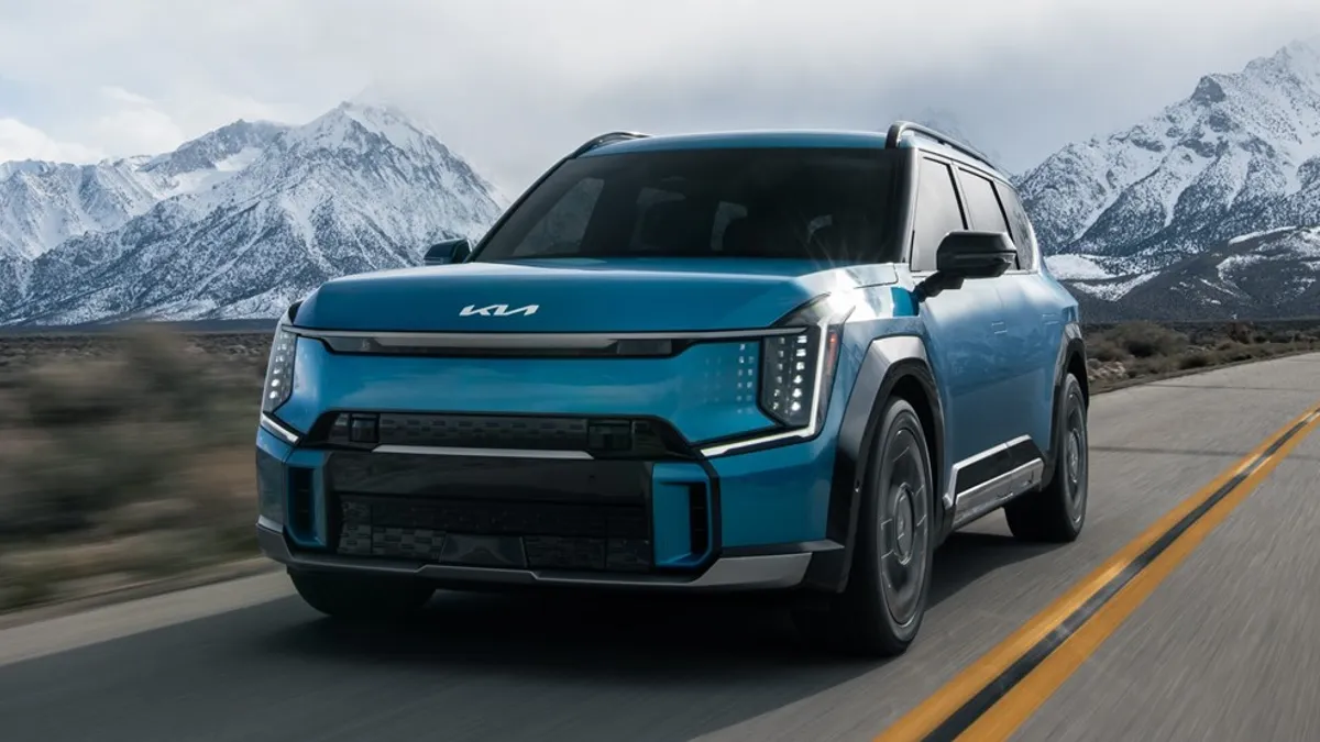 A blue 2024 Kia EV9 SUV on the road with snow-capped mountains in the background.