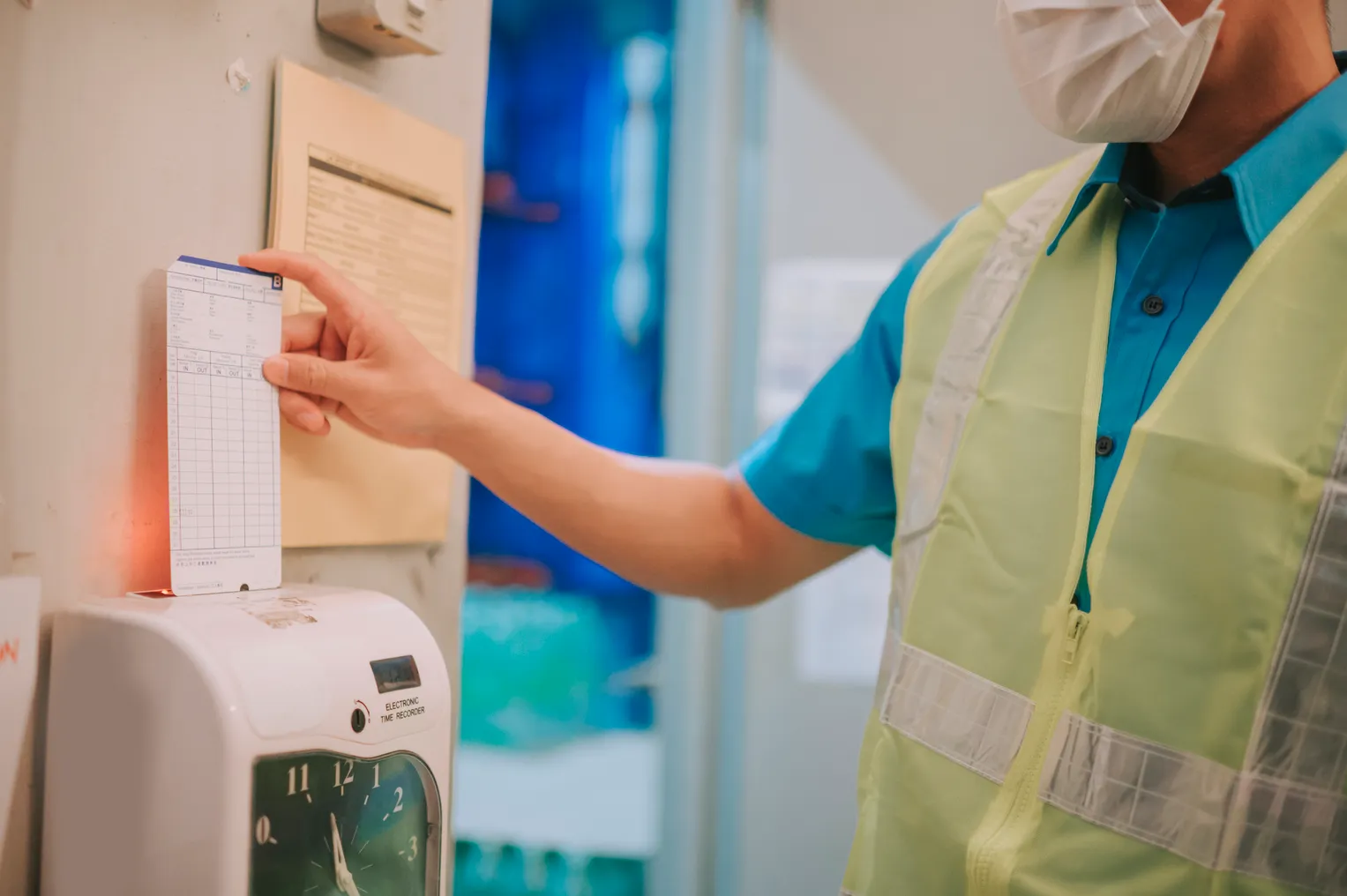 A worker in a safety vests uses a time card machine.