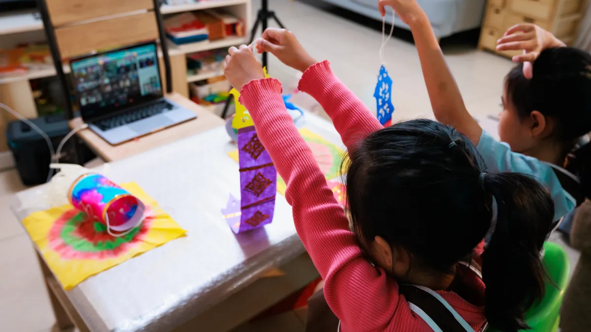 Children show their finishished work to teacher and friend while online learning.