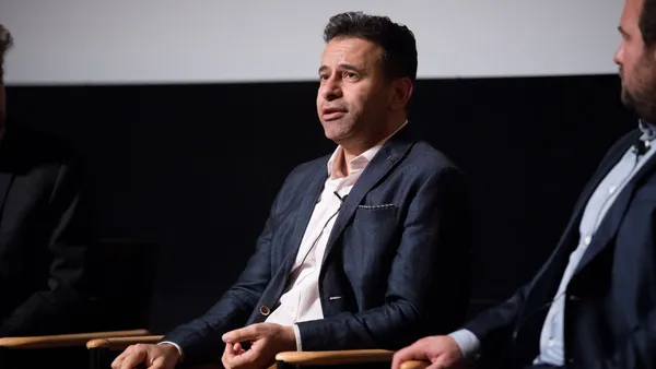 A person in a dark suit speaks on stage during a film screening.