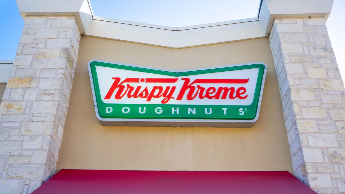 An image of a beige building with a green sign that says "Krispy Kreme" in red and then "doughnuts" in white typeface.