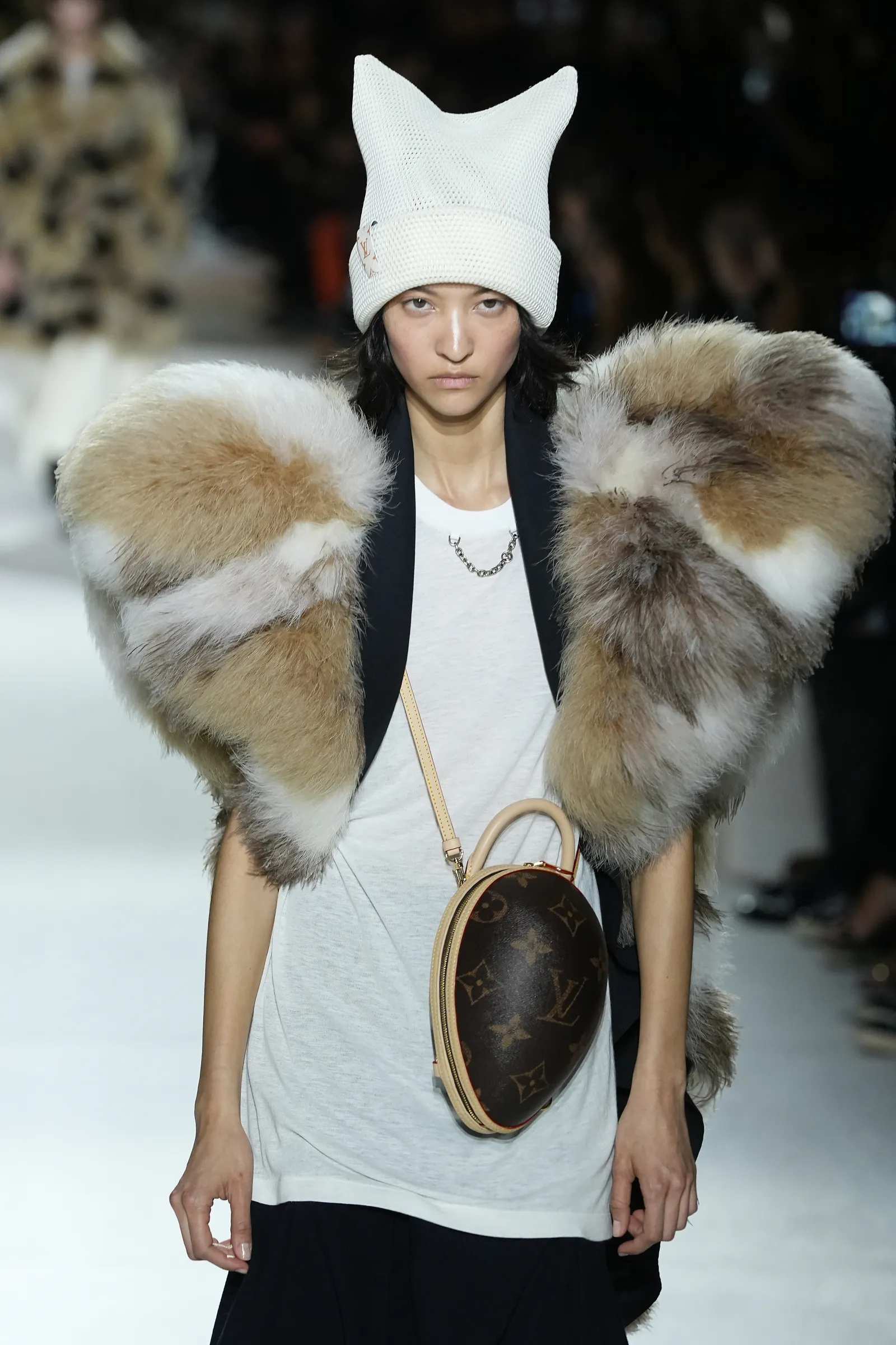 A model in a fur-shouldered top and a pointed hat walks the runway.