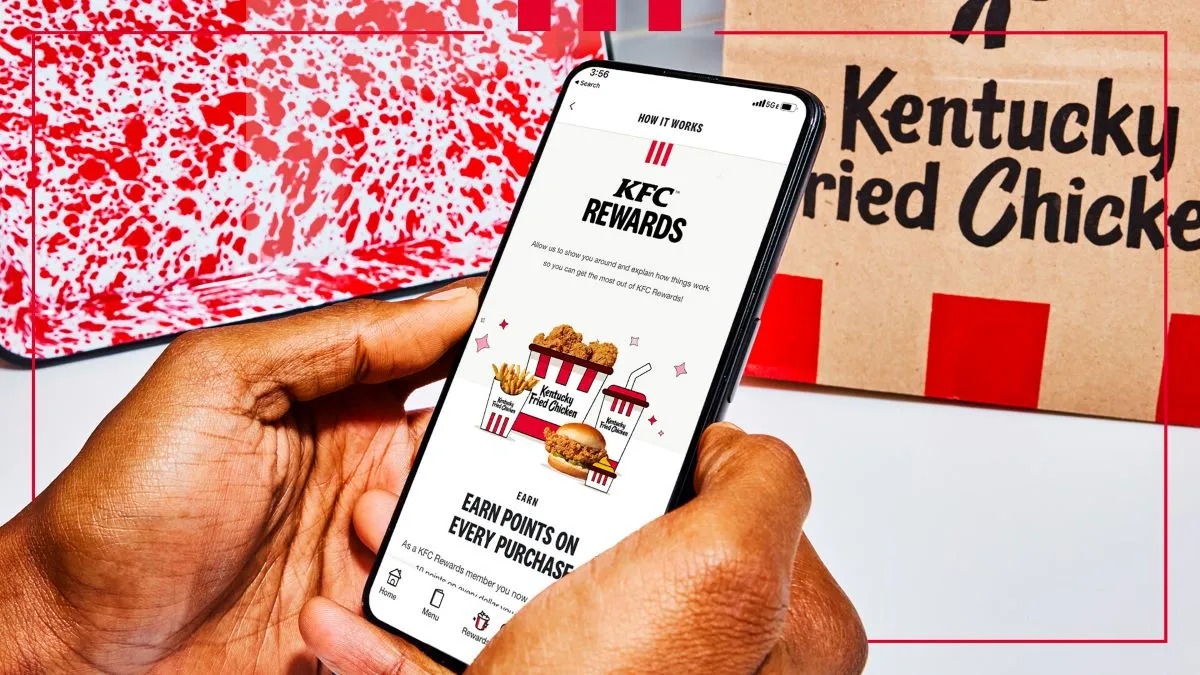 An image of a hand holding a smart phone with a KFC Rewards logo on the screen