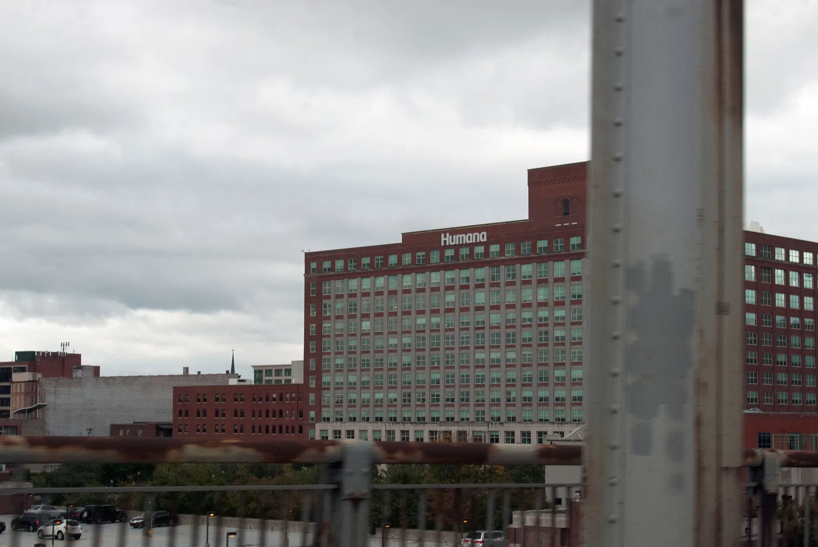 A red-brick mid-rise office building with rows of windows and a “Humana” sign on the roof, seen under a cloudy gray sky.