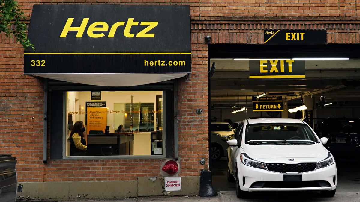 Car pulling out of garage under banner with Hertz logo