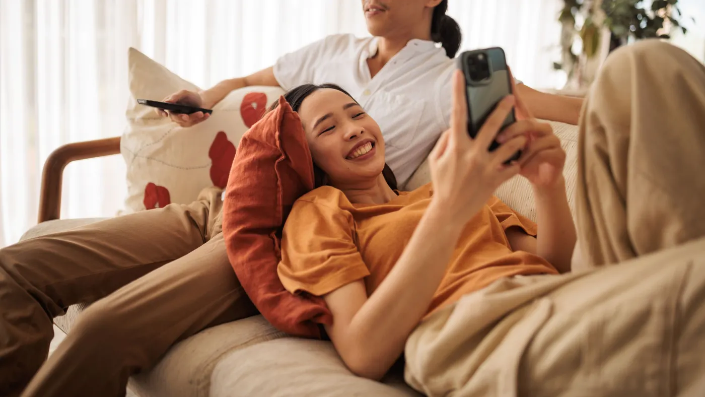 A person checks their phone while leaning on their partner on a living room couch