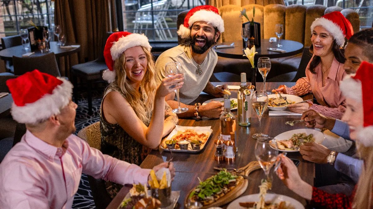 An image of six people at a table in a restaurant wearing Santa hats