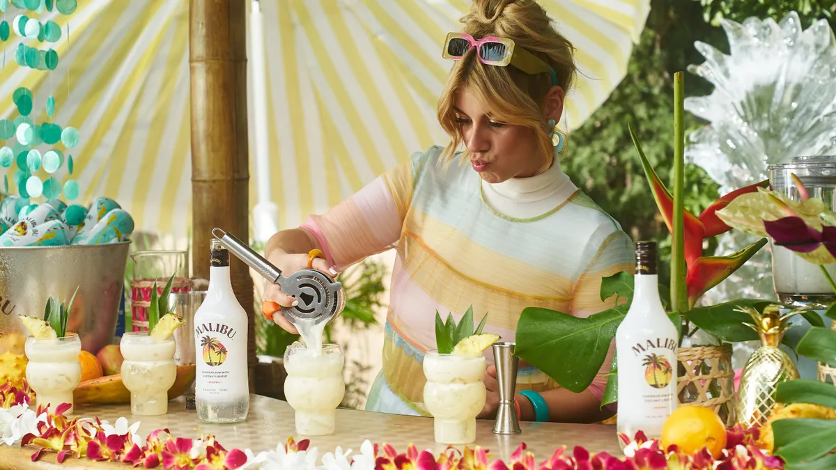 A person pours cocktails behind a brightly colored bar.