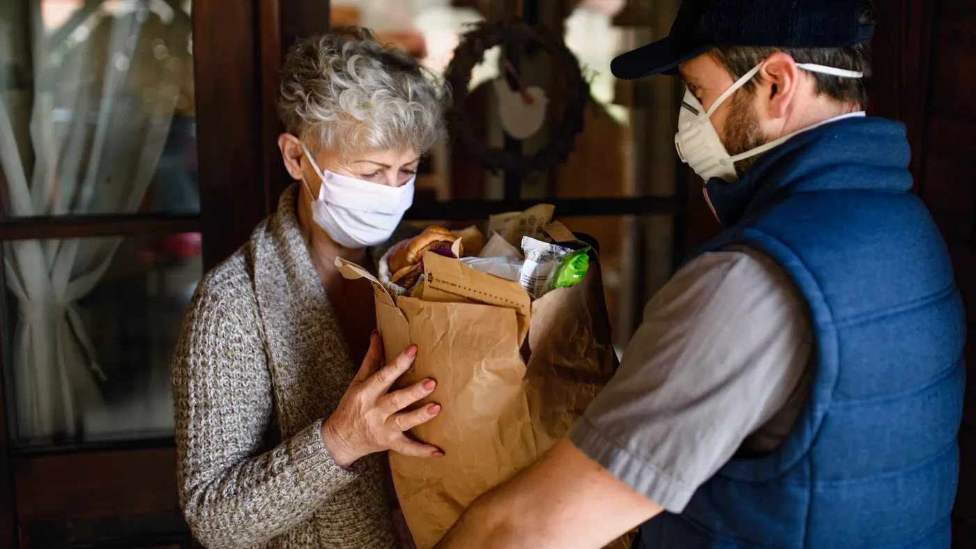 Courier delivering shopping to senior woman with face mask, corona virus and quarantine concept.