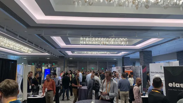 A crowd of people in business and business-casual clothes wander around an open space filled with booths for companies that represent construction technology firms.
