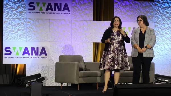 Two people stand on a stage during an event. Behind them is a backdrop that includes the SWANA logo.