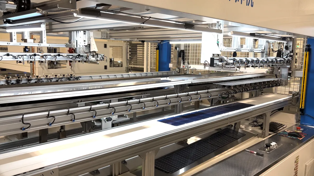 Two silver assembly lines with solar panels in a beige factory room.