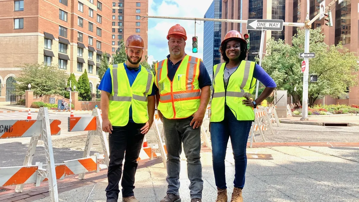 Three construction workers pose on a city street in work vests