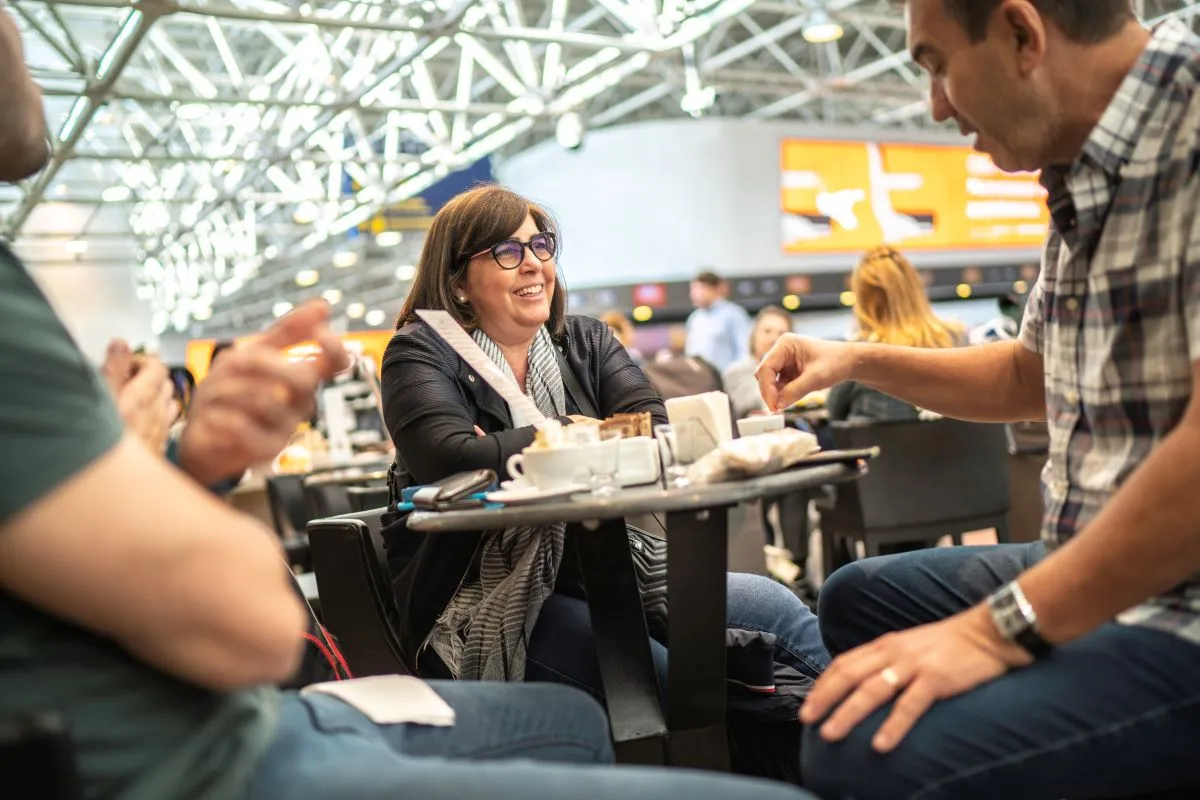 An image of a woman with glasses and a man eating at a table in an airport.