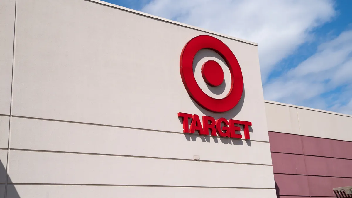 A red bullseye logo with the word Target underneath decorates a storefront against a bright blue sky with puffy white clouds.