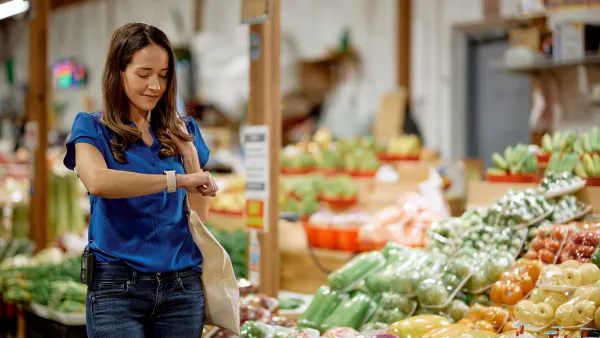 A person looks at a smartwatch while walking past packaged produce.