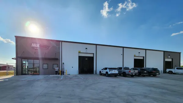 With the sun shining brightly behind it, a one-story building sits in the center of the photo, shadowed. The word "McKinstry" is visible above a door on the left.