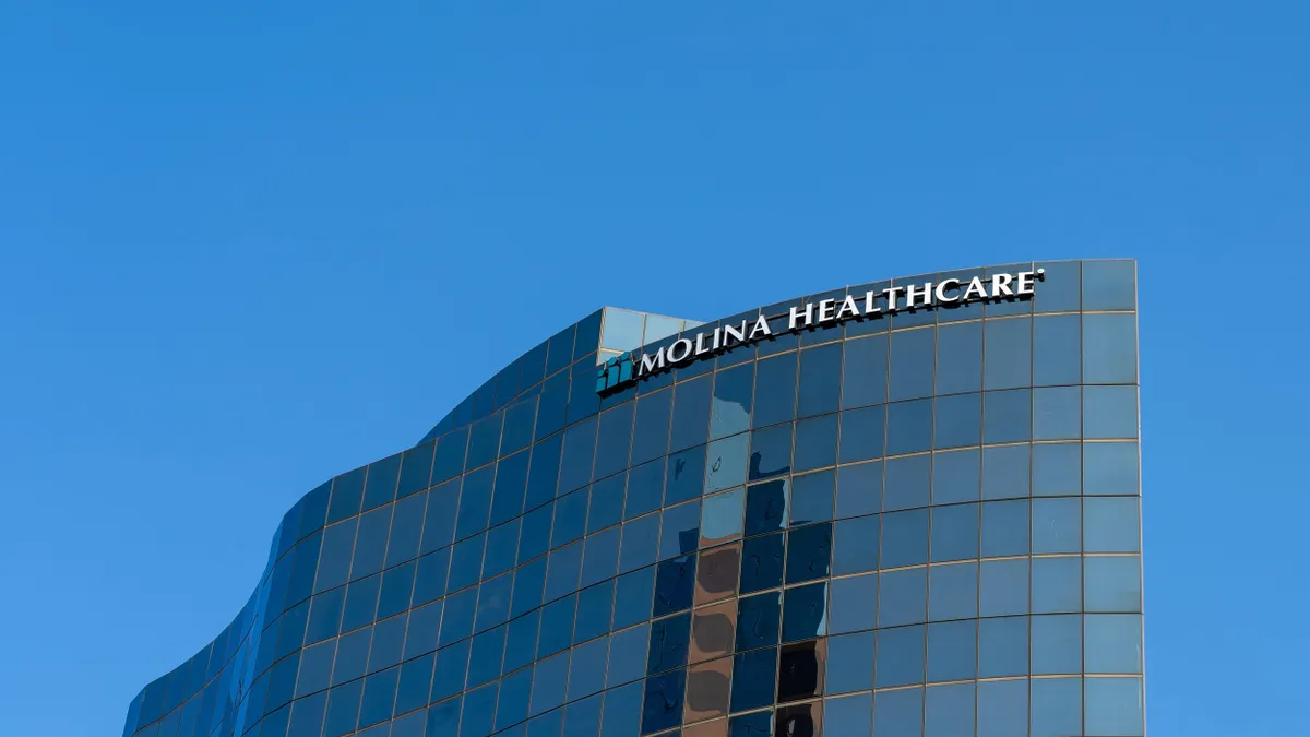A modern, curved office tower with reflective blue glass windows and the words "Molina Healthcare" displayed at the top. The sky is clear and bright blue.