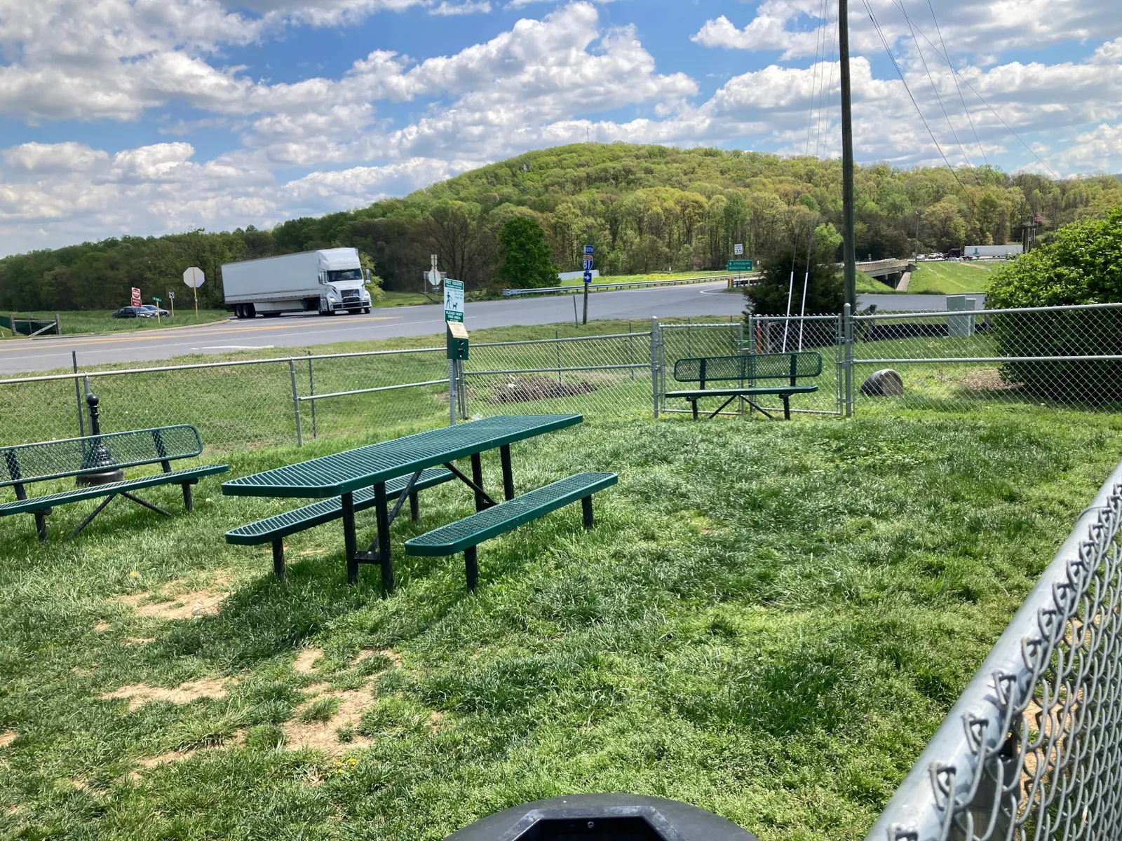 A photo of a fenced in dog park with benches and a picnic table, along with a waste receptacle.