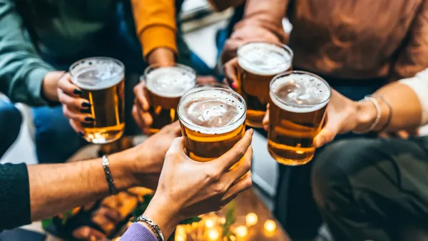 A closeup of five people's arms holding beer glasses.
