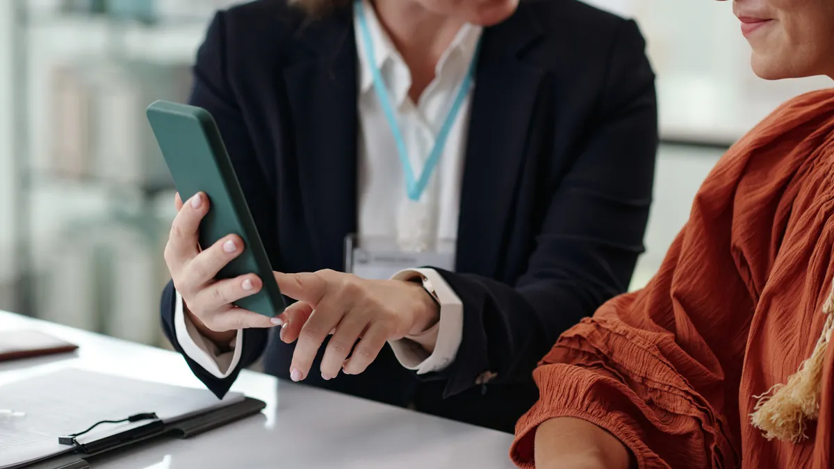 A person shows online registration to another person on mobile phone while they sitting in office